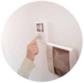 Doigt appuyant sur un thermostat mural à côté d'un interrupteur sur un mur blanc