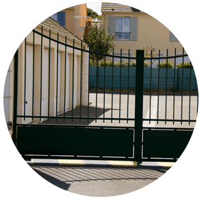 Portail métallique vert devant une maison et une cour ensoleillées, vu de la rue.