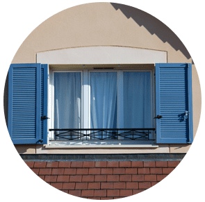 Volets bleus encadrant une fenêtre aux rideaux fermés sur une façade d'immeuble beige