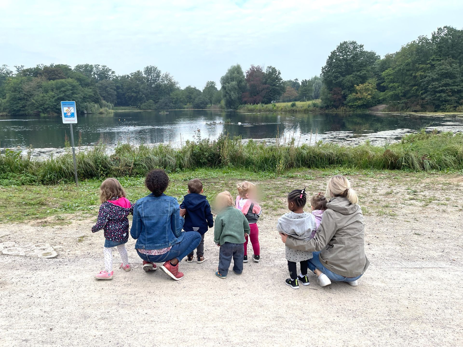 Eine Gruppe von Menschen sitzt auf dem Boden und schaut auf einen See.