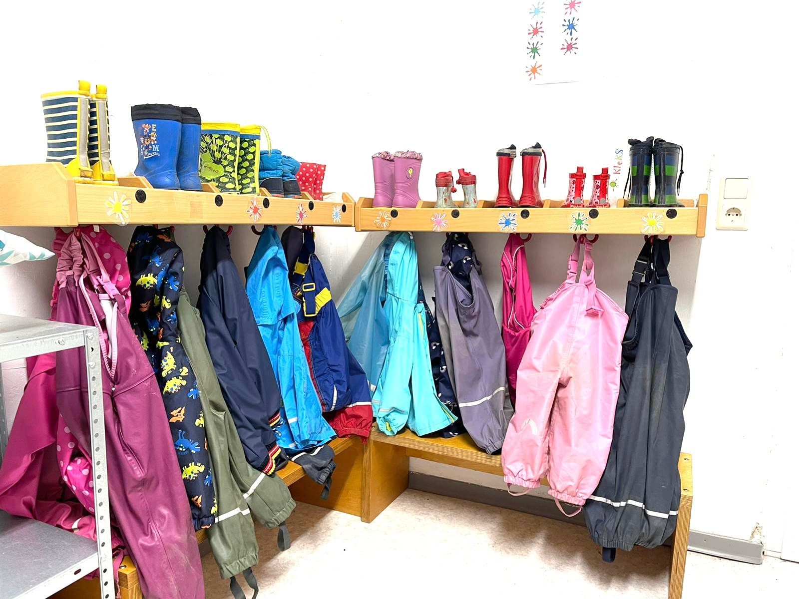 Eine Reihe von Jacken und Gummistiefeln hängt an einem Ständer in einer Umkleidekabine.