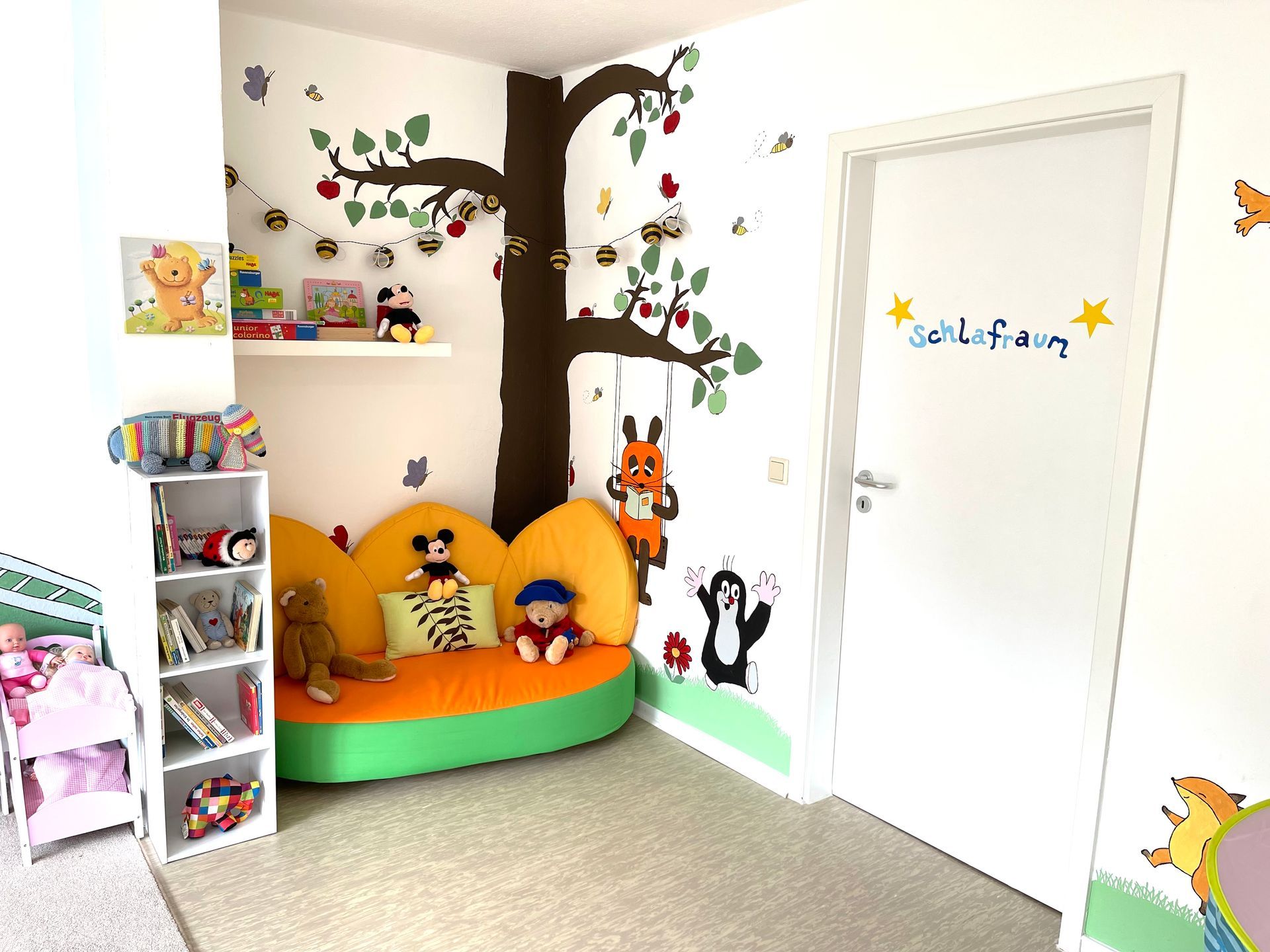 Ein Kinderzimmer mit einem Sofa und einem Baum an der Wand.