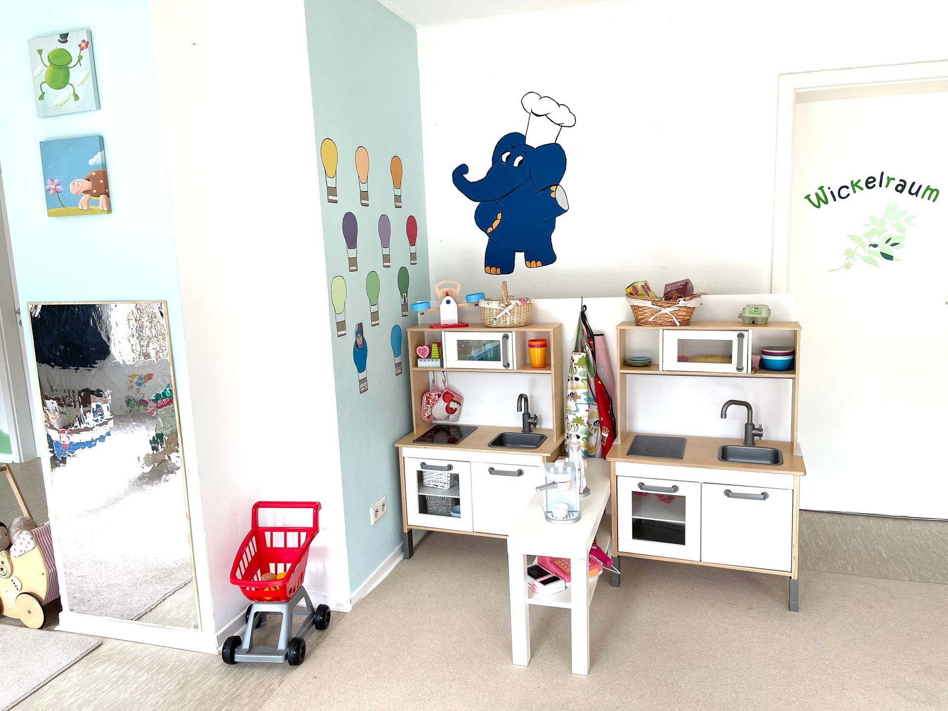 Ein Raum mit zwei Spielküchen und einem Einkaufswagen.