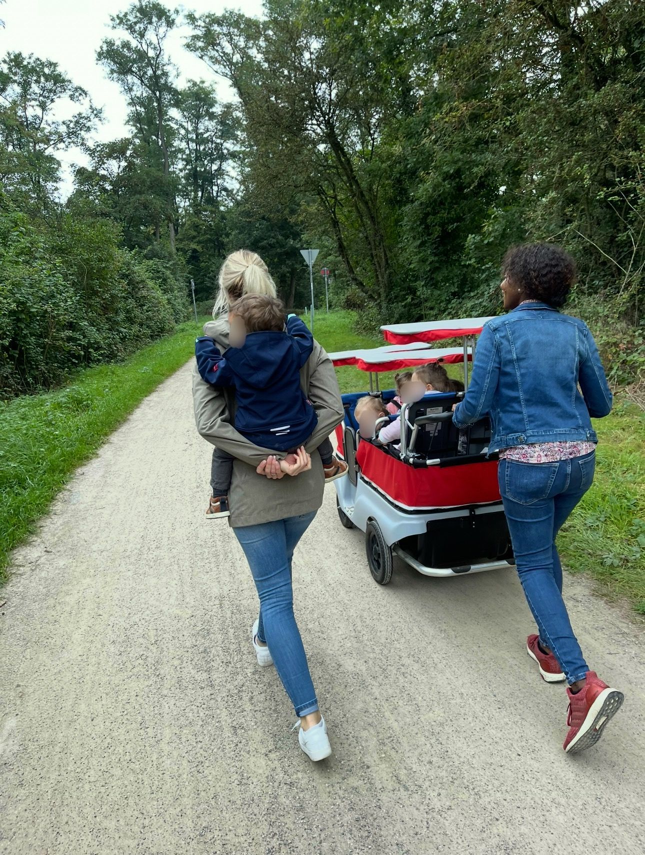 Eine Frau schiebt einen Wagen mit einem Kind darin einen Feldweg entlang.