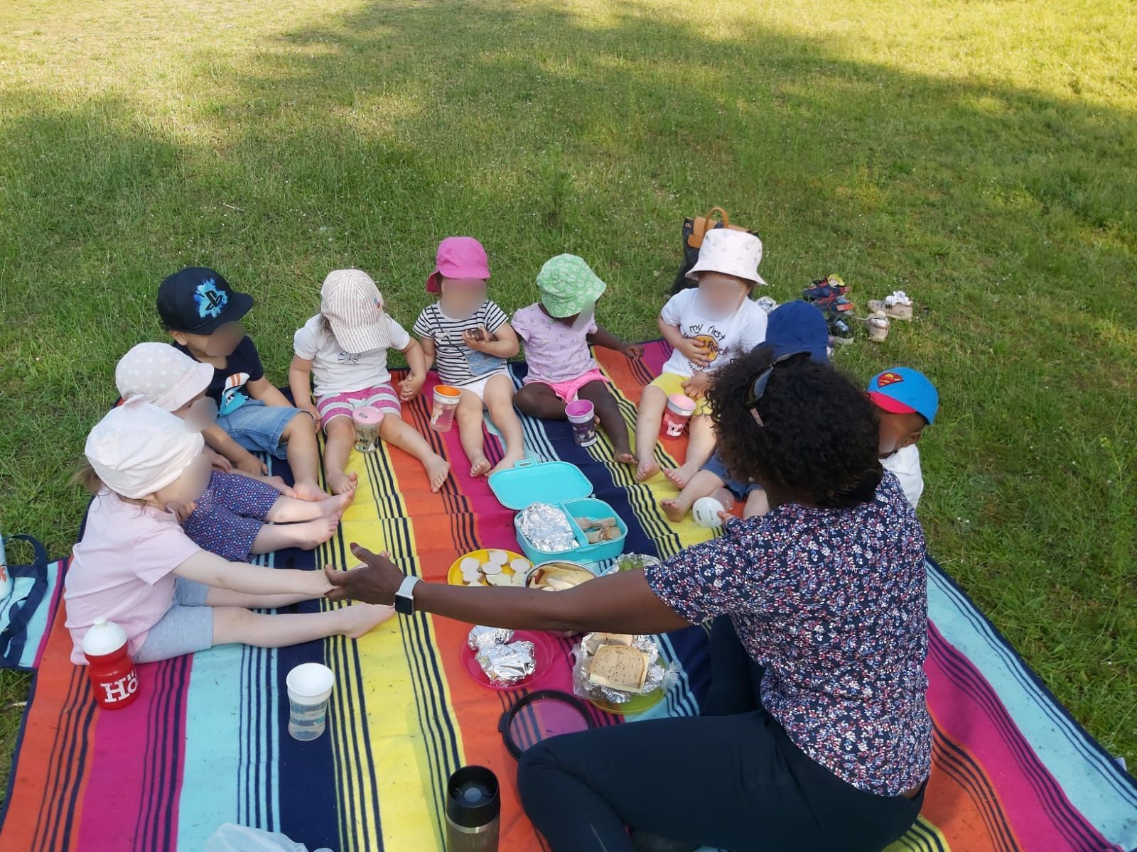 Eine Gruppe Kinder sitzt auf einer Decke im Gras.