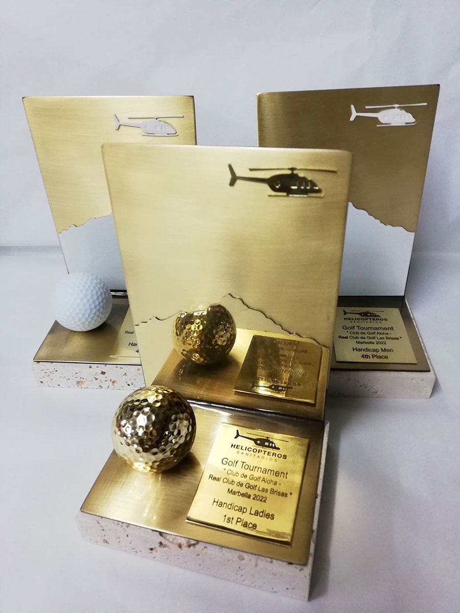 Sobre una mesa hay tres trofeos de oro con un helicóptero encima.