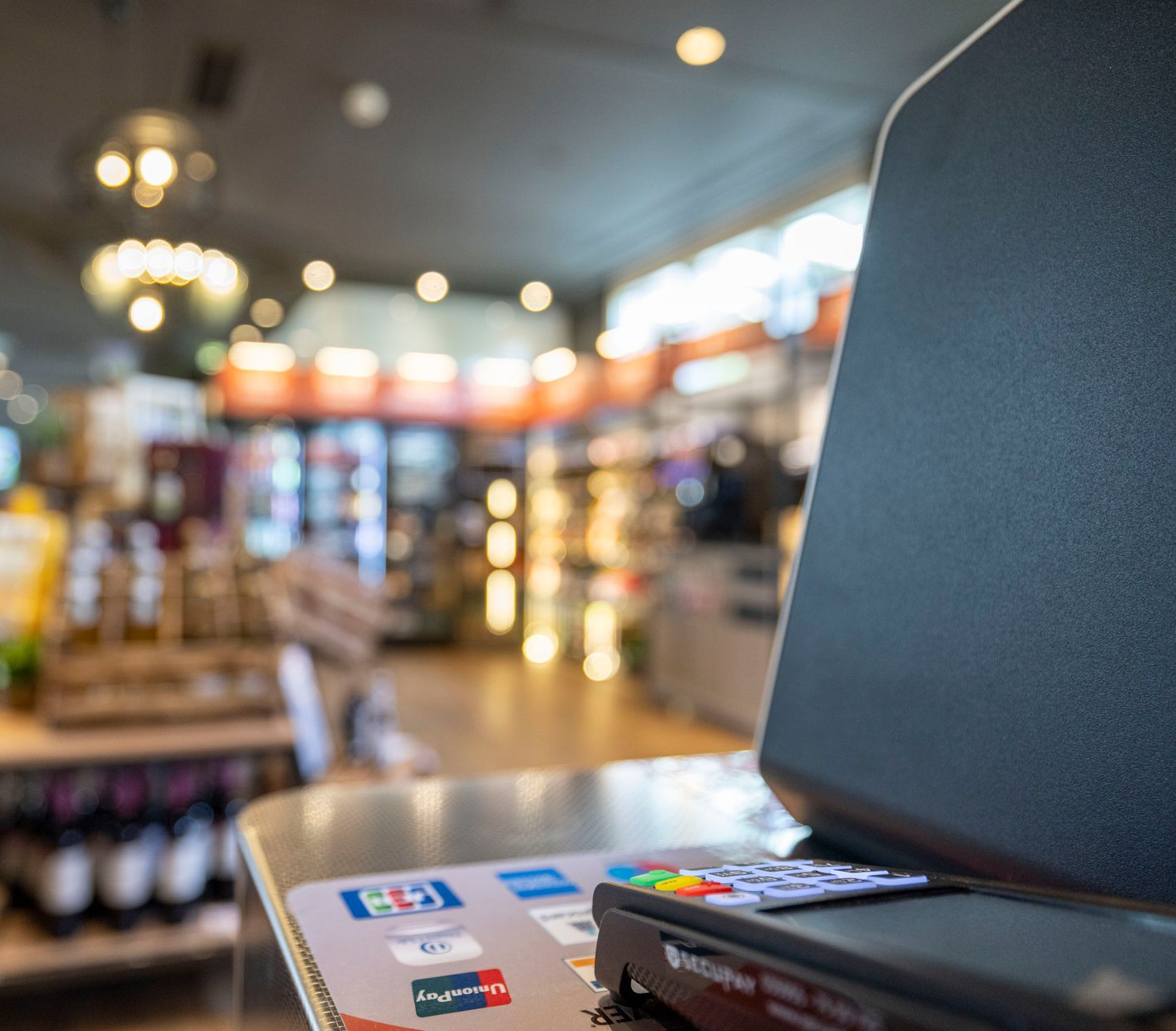 Zahlungsterminal auf der Ladentheke vor verschwommenem Hintergrund mit Regalen und Produkten.