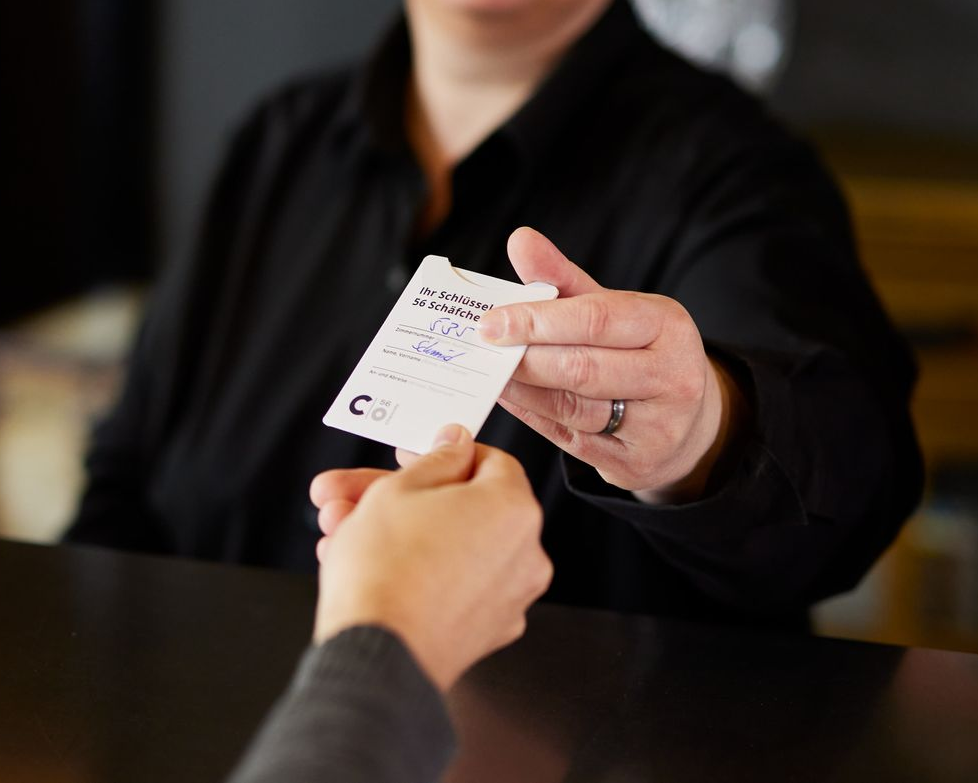 Frau hält gefaltete weiße Handtücher in einem Hotelzimmer vor einer Wandmalerei im Industriestil.