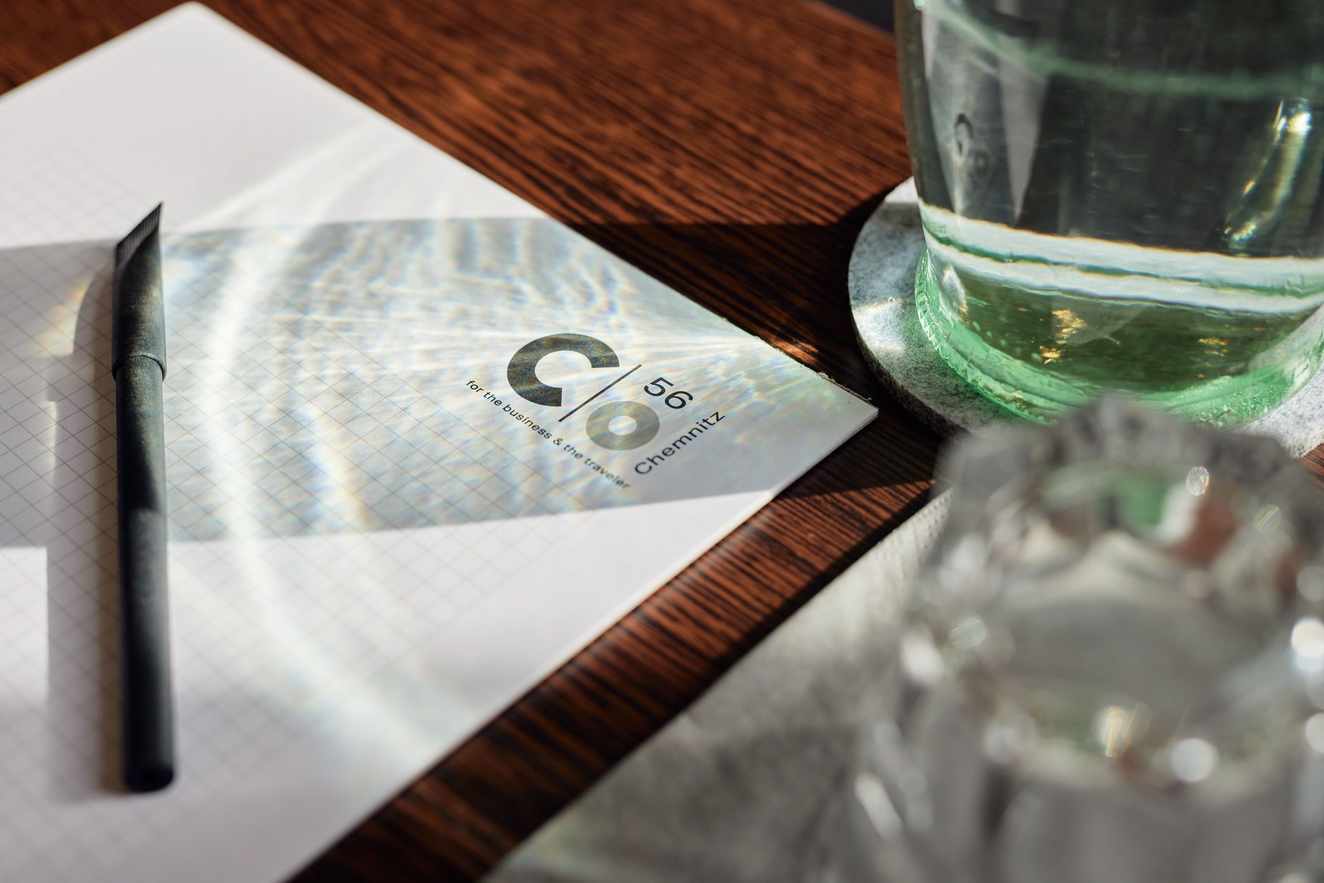 Zwei Männer genießen ihr Frühstück, einer lächelt beim Zeitunglesen, Croissants und Saft stehen auf dem Tisch.