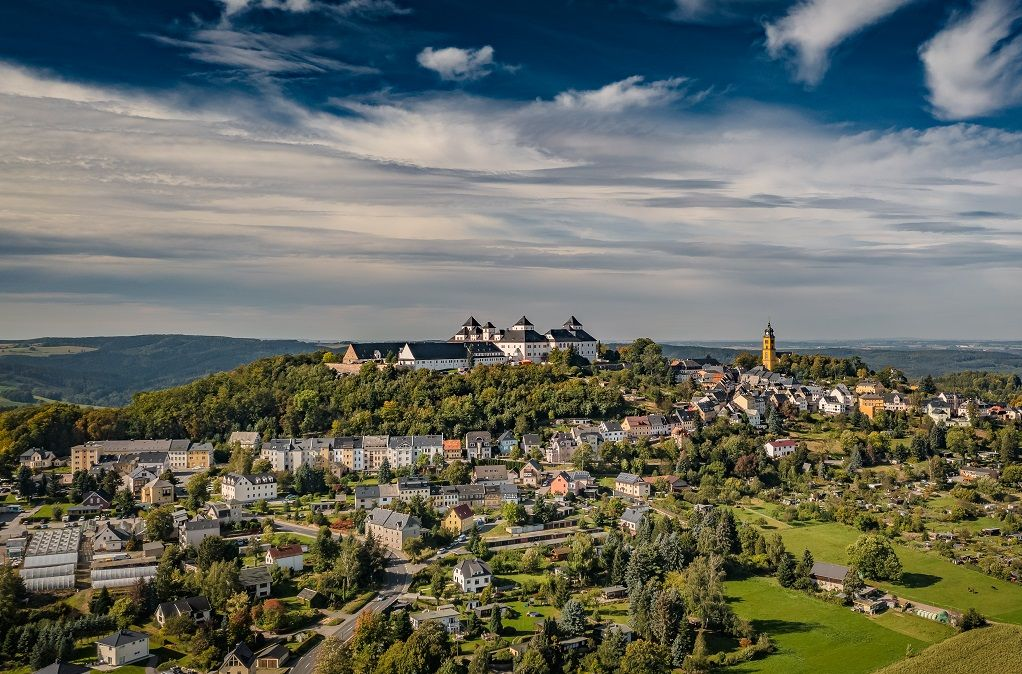 Eine Stadt mit Gebäuden und einer Burg auf einem Hügel unter bewölktem Himmel.
