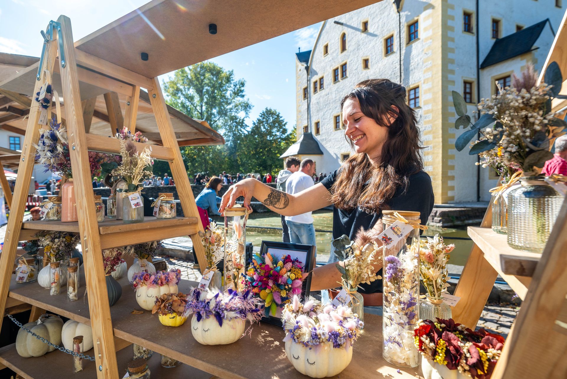 Eine lächelnde Frau verkauft an einem STand handgemachte Geschenke vor dem Wasserschloss Klaffenbach