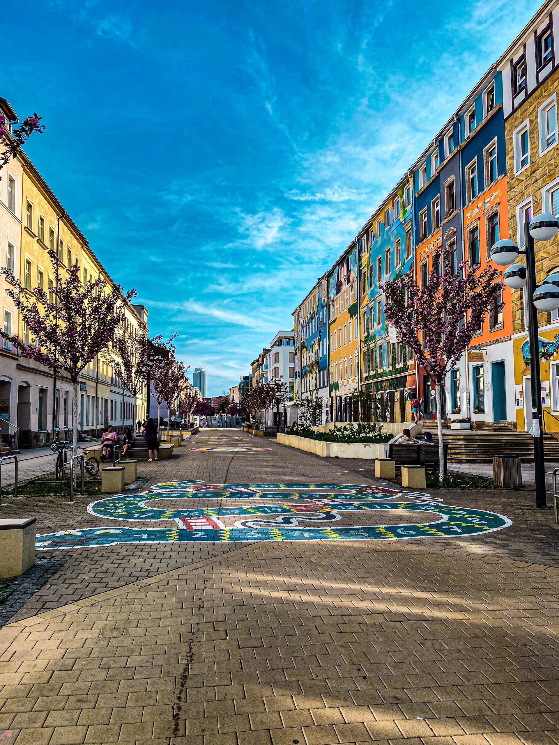 Farbenfrohes Wandgemälde auf einem gepflasterten Platz zwischen historischen Gebäuden unter strahlend blauem Himmel