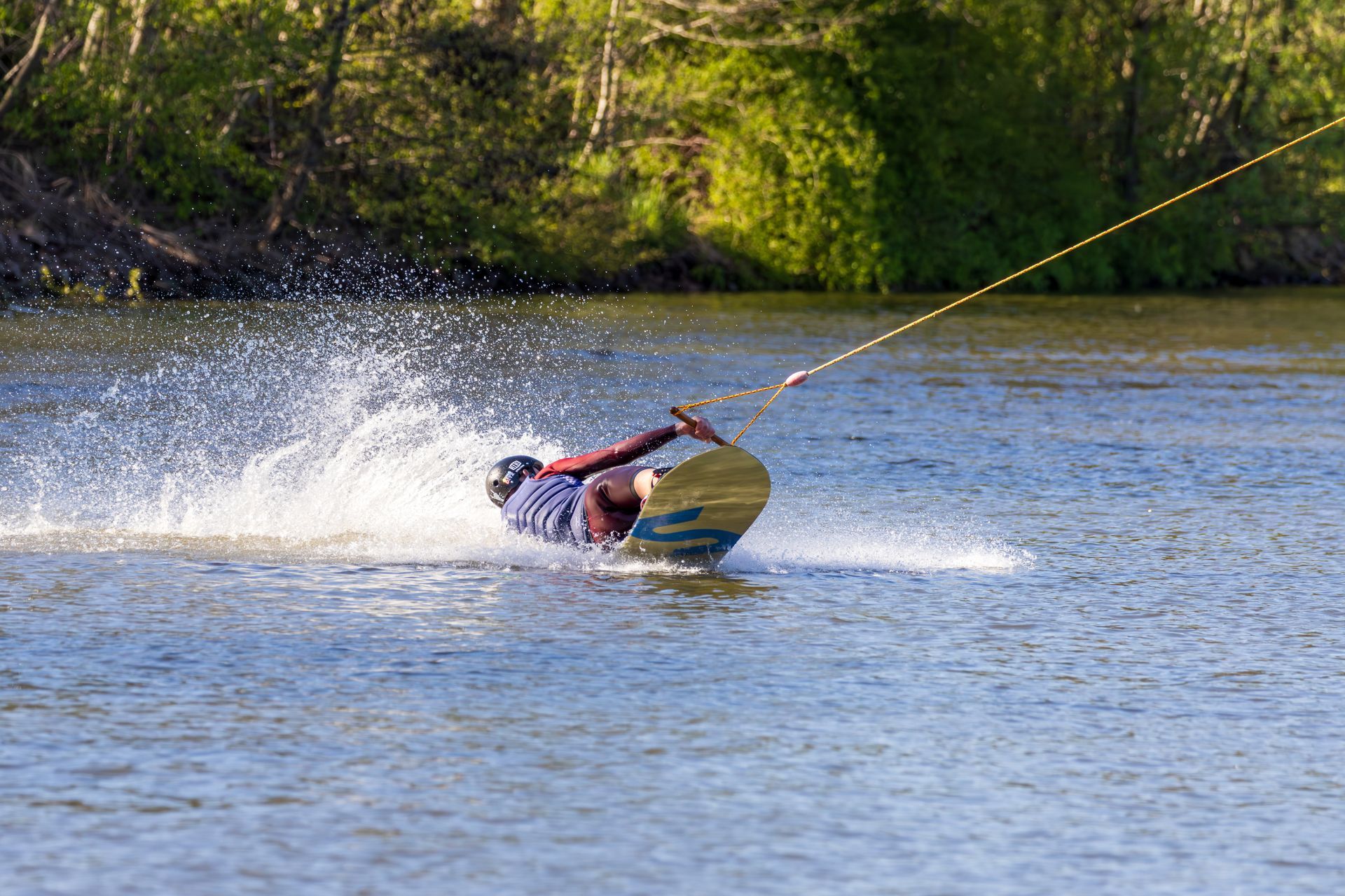 Ein Wakeboarder, der über einen See gleitet und in der Nähe eines bewaldeten Ufers Wasser aufwirbelt