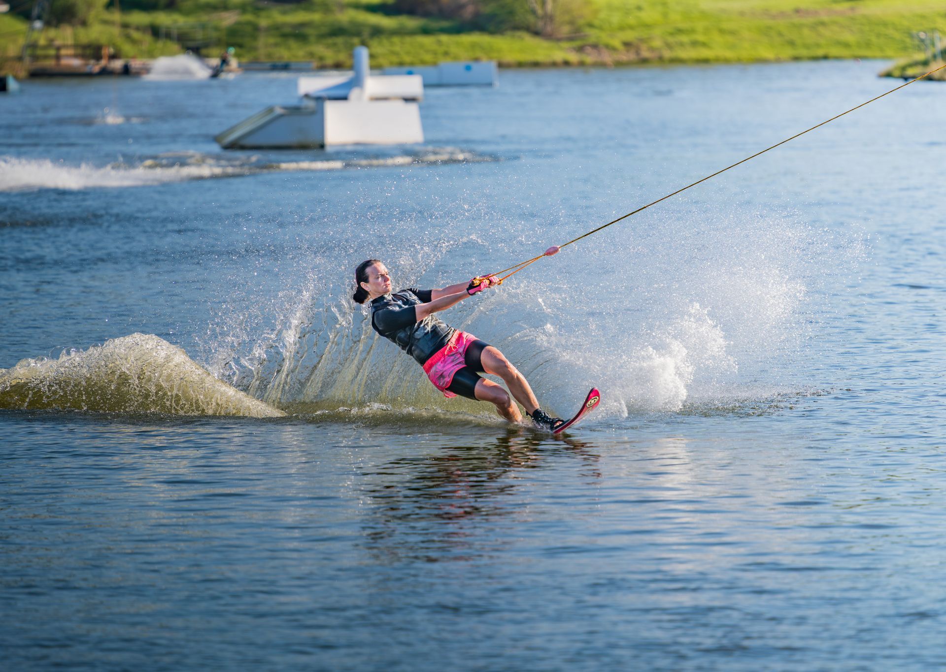Ein Wakeboarder, der über einen See gleitet und dabei in der Nähe eines schwimmenden Hindernisses eine Wasserspritzer hinter sich hinterlässt