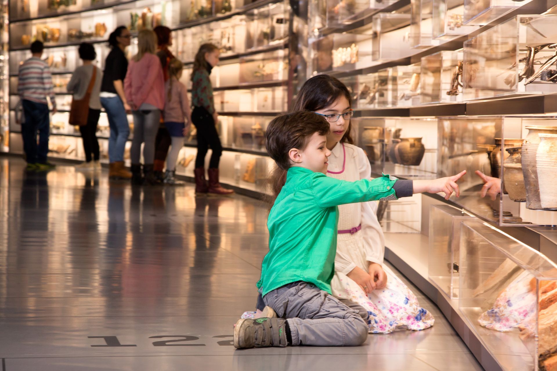 2 Kinder knien vor einer großen Vitrine mit Exponaten im smac.