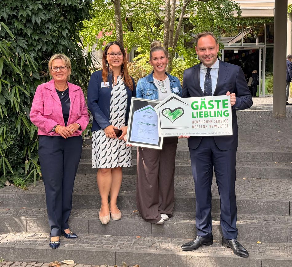 Vier Personen stehen im Freien und halten eine Urkunde und ein Schild mit der Aufschrift „GÄSTE LIEBLING“.