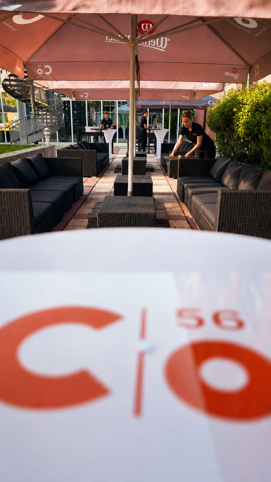 Terrasse des Konferenzbereiches im c/o56 Chemnitz mit Korbmöbeln, Sonnenschirmen und einem weißen Tisch im Vordergrund.