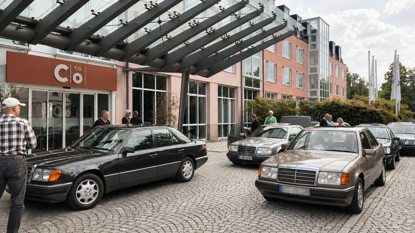 Vor dem Eingang eines modernen Gebäudes mit Glasvordach standen mehrere schwarze Autos.