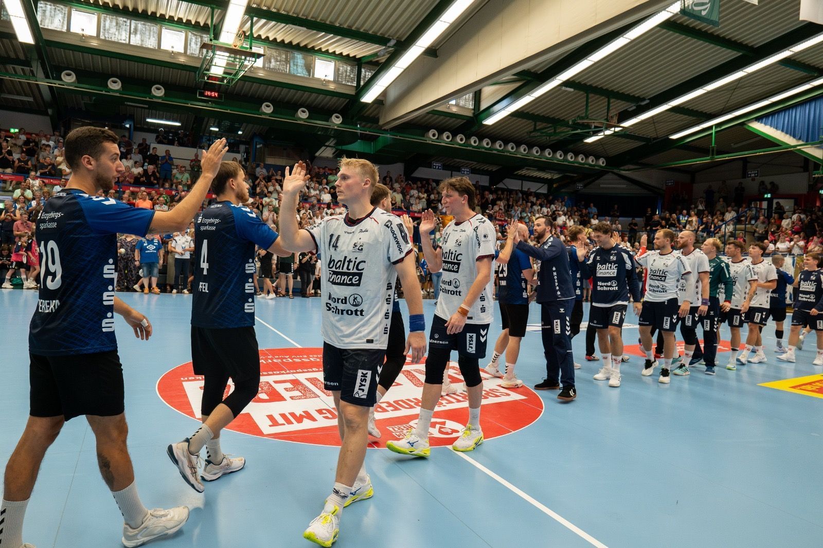 Die Handballmannschaften stellen sich nach dem Spiel auf einem Hallenfeld auf, um sich die Hände zu 