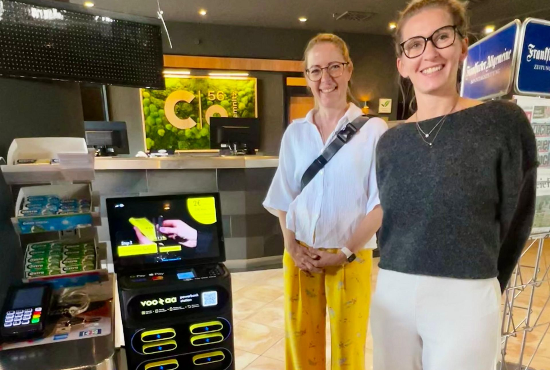 Zwei Personen stehen an der Kasse des Hotelshops im c/o56 neben einem Powerbank Automaten.