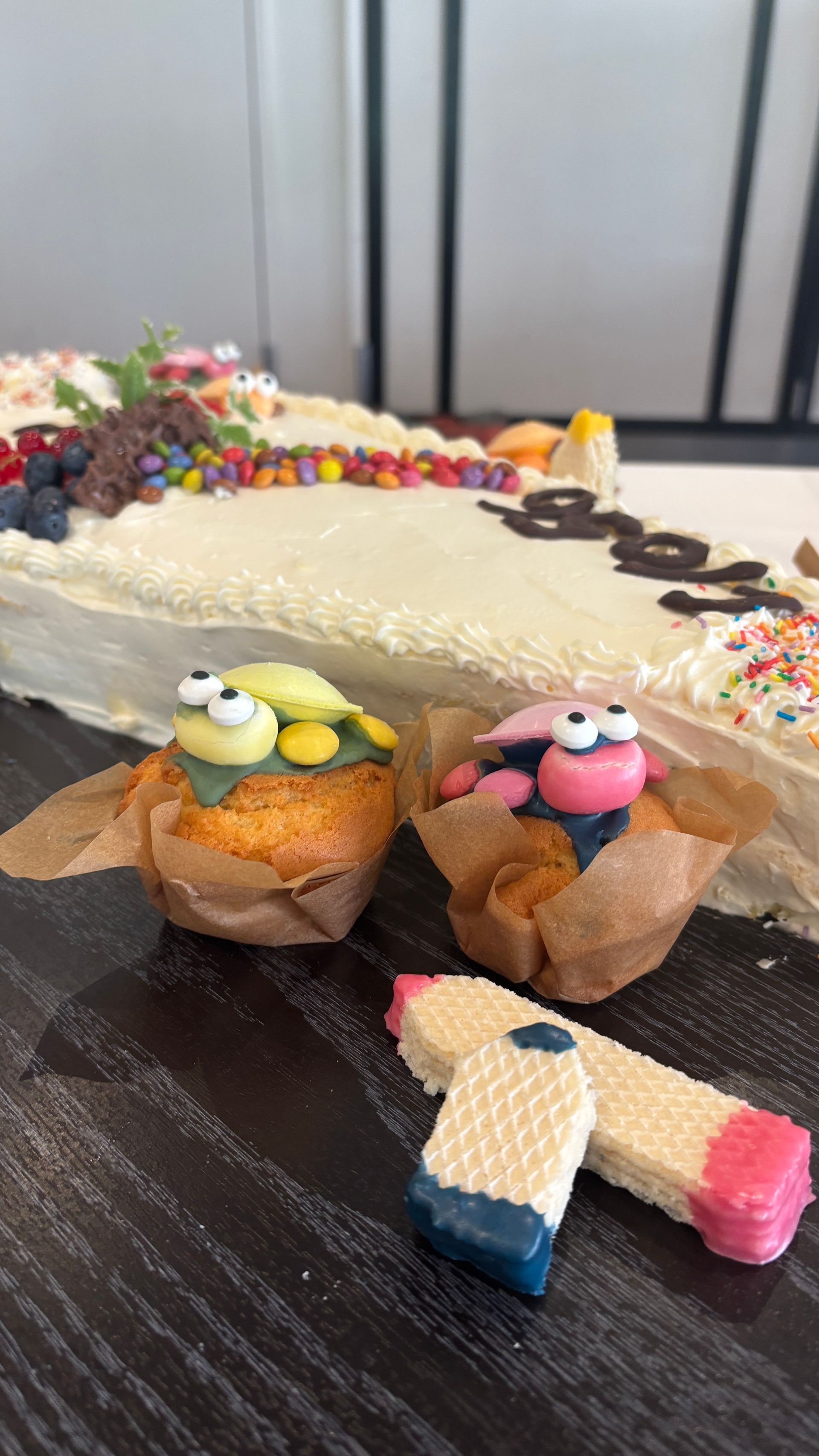Ein kleiner, dekorierter Kuchen mit zwei Zuckerfiguren in Cupcakes und einem kleinen rosa-weiß-blauen Bonbon auf einem Tisch