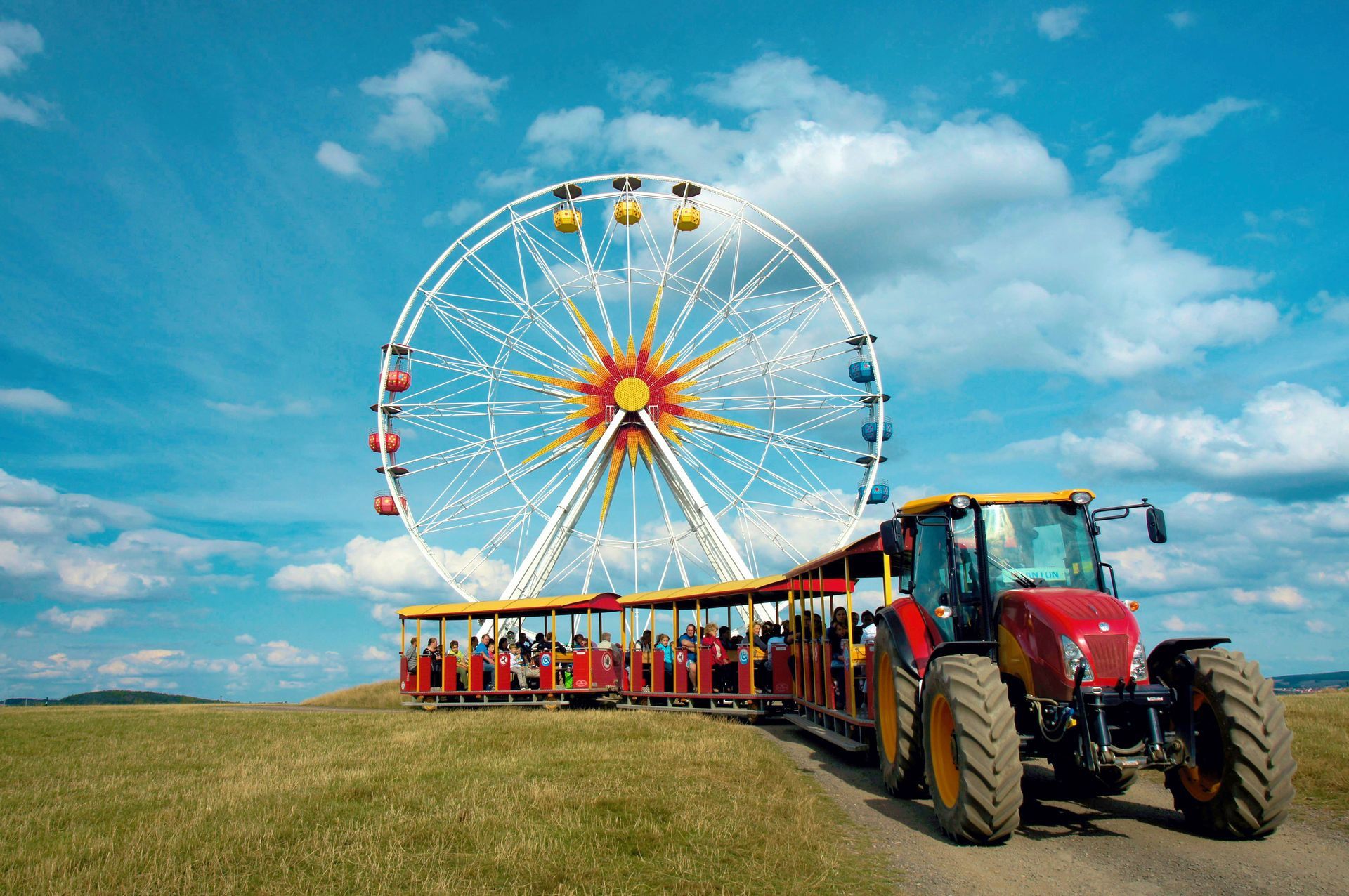 Riesenrad und Fahrt mit einem roten Traktor auf einer Wiese unter blauem Himmel