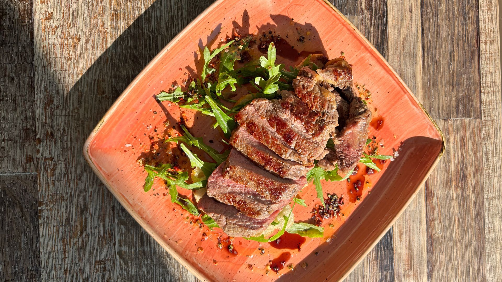 Gegrilltes Steak in Scheiben mit Gemüse auf einem quadratischen orangefarbenen Teller auf einem Holztisch