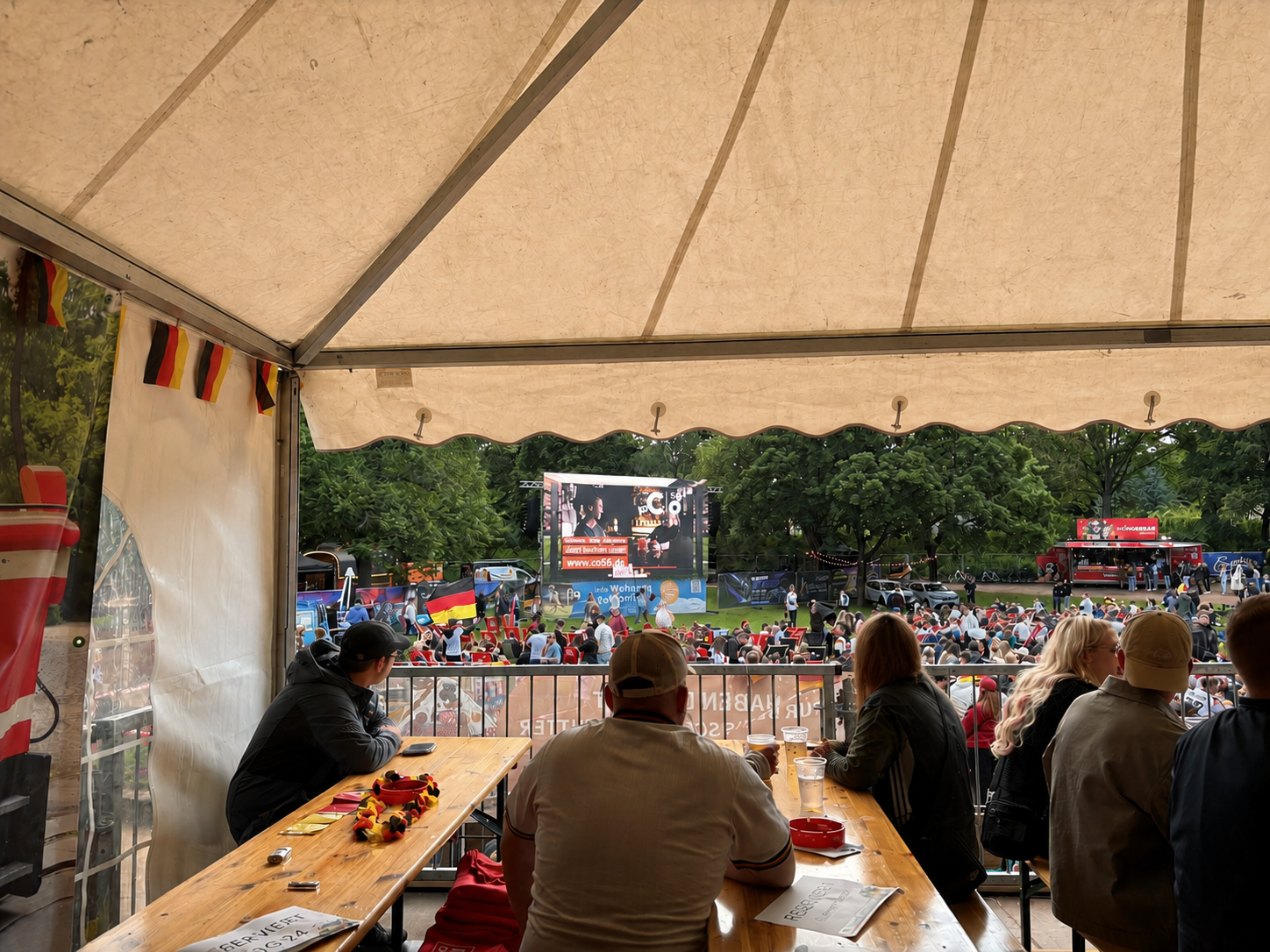 Menschen sitzen unter einem Zelt und verfolgen eine Live-Veranstaltung im Freien.