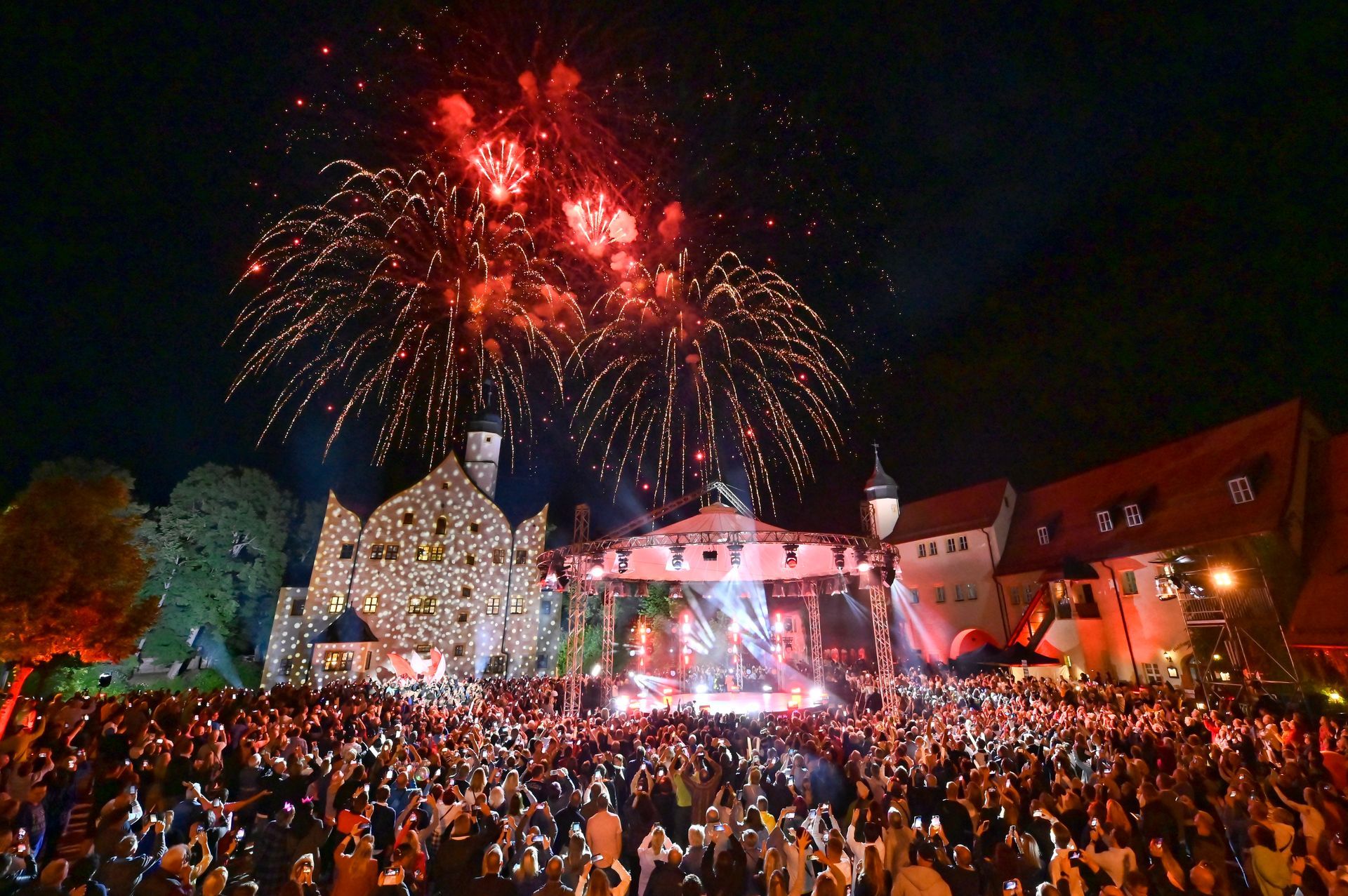 Vor dem Wasserschloss KLaffenbach steht eine beleuchtete Bühne über der ein Feuerwerk explodiert.