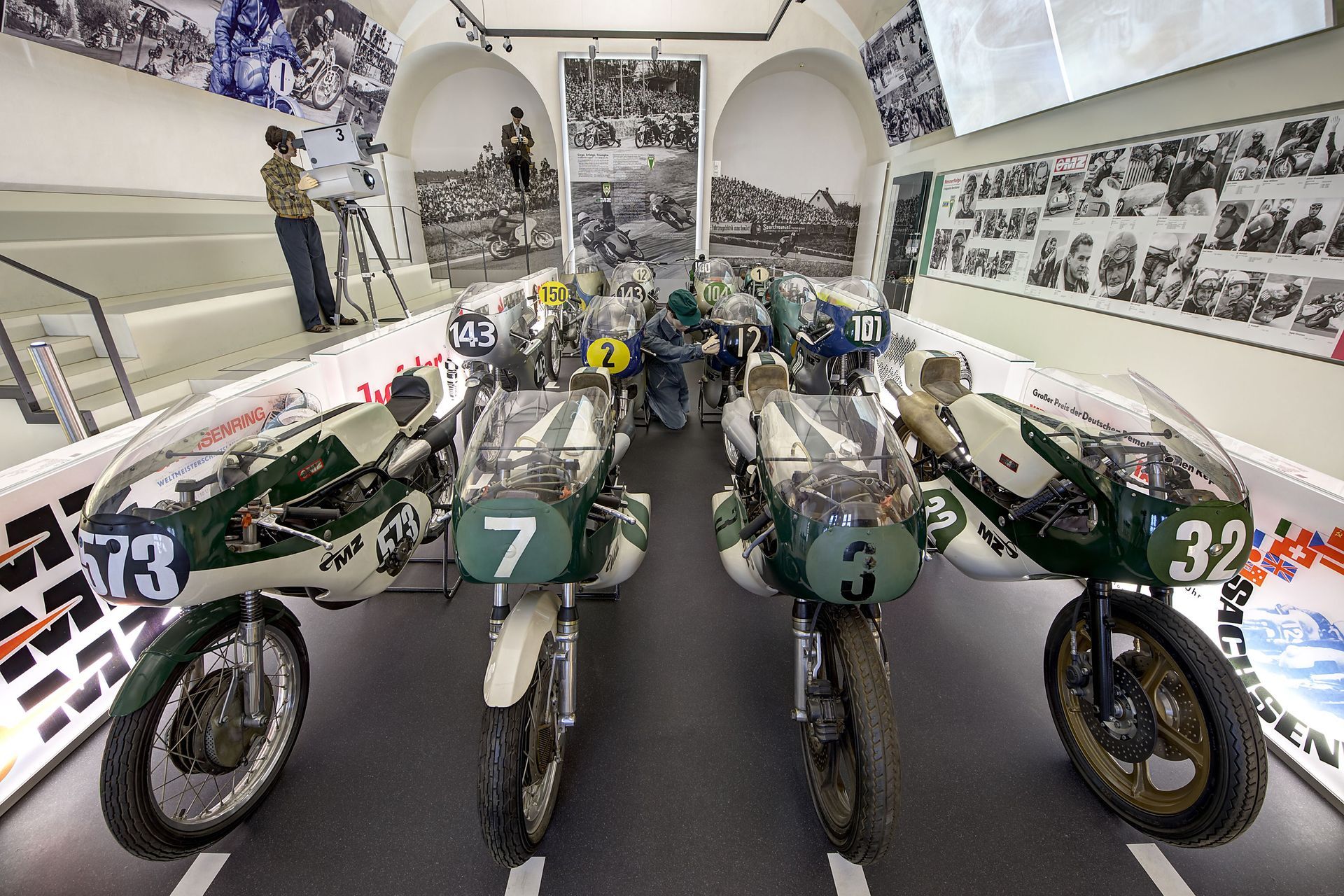 Motorräder, grüne und weiße Rennmaschinen, in einer Museumsausstellung.