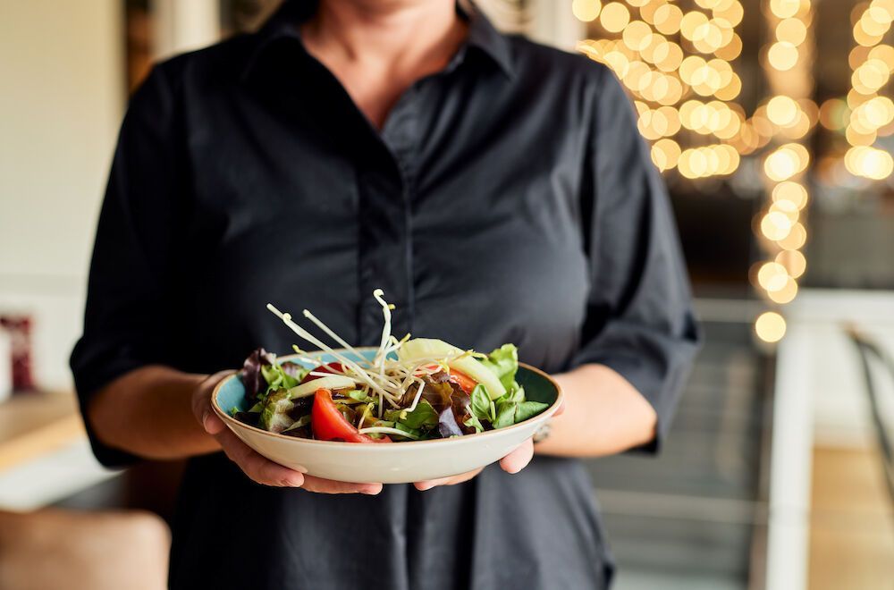 Eine Kellnerin in einem Restaurant hält eine Schüssel Salat in der Hand; die Person trägt ein schwarzes Hemd.