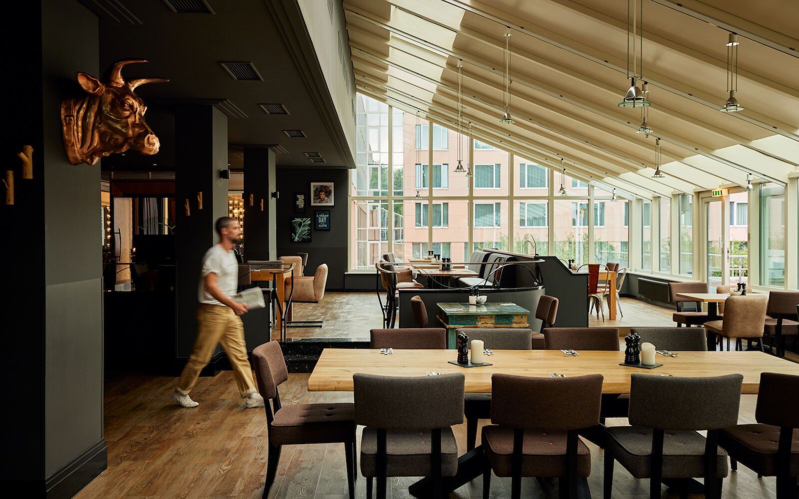 Restaurantinterieur mit einem vorbeigehenden Mann, Tischen mit Stühlen und einem großen Fenster.