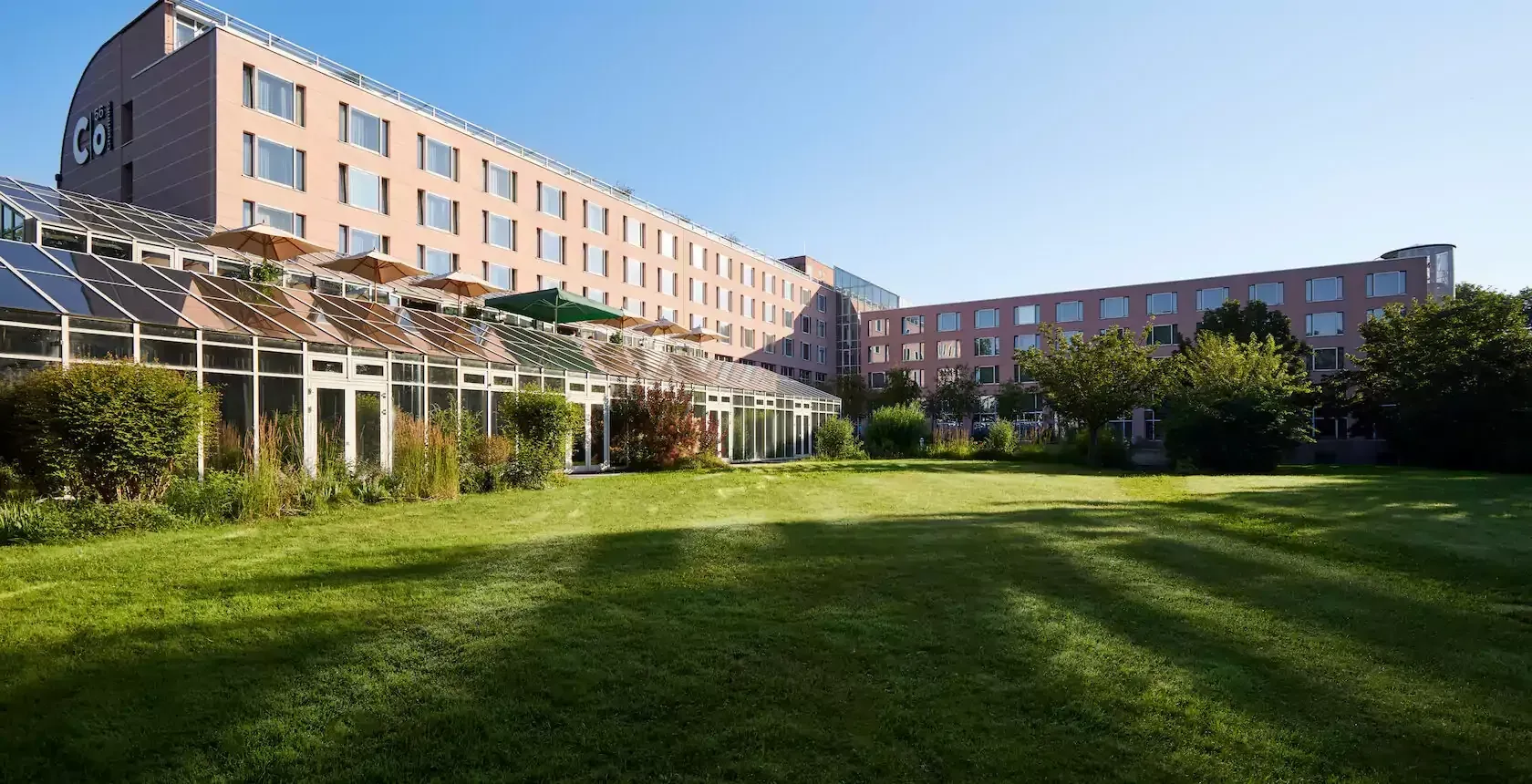 c/onsum56 Üppiger grüner Rasen vor einem modernen mehrstöckigen Hotel mit gläsernem Wintergarten.