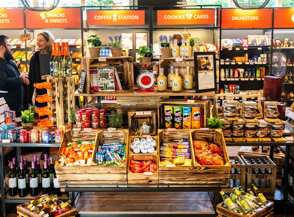 Auslage mit Gourmet-Snacks in einem Geschäft, mit Regalen voller Süßigkeiten, Kekse, Pralinen und Schildern für die Kaffeeecke.