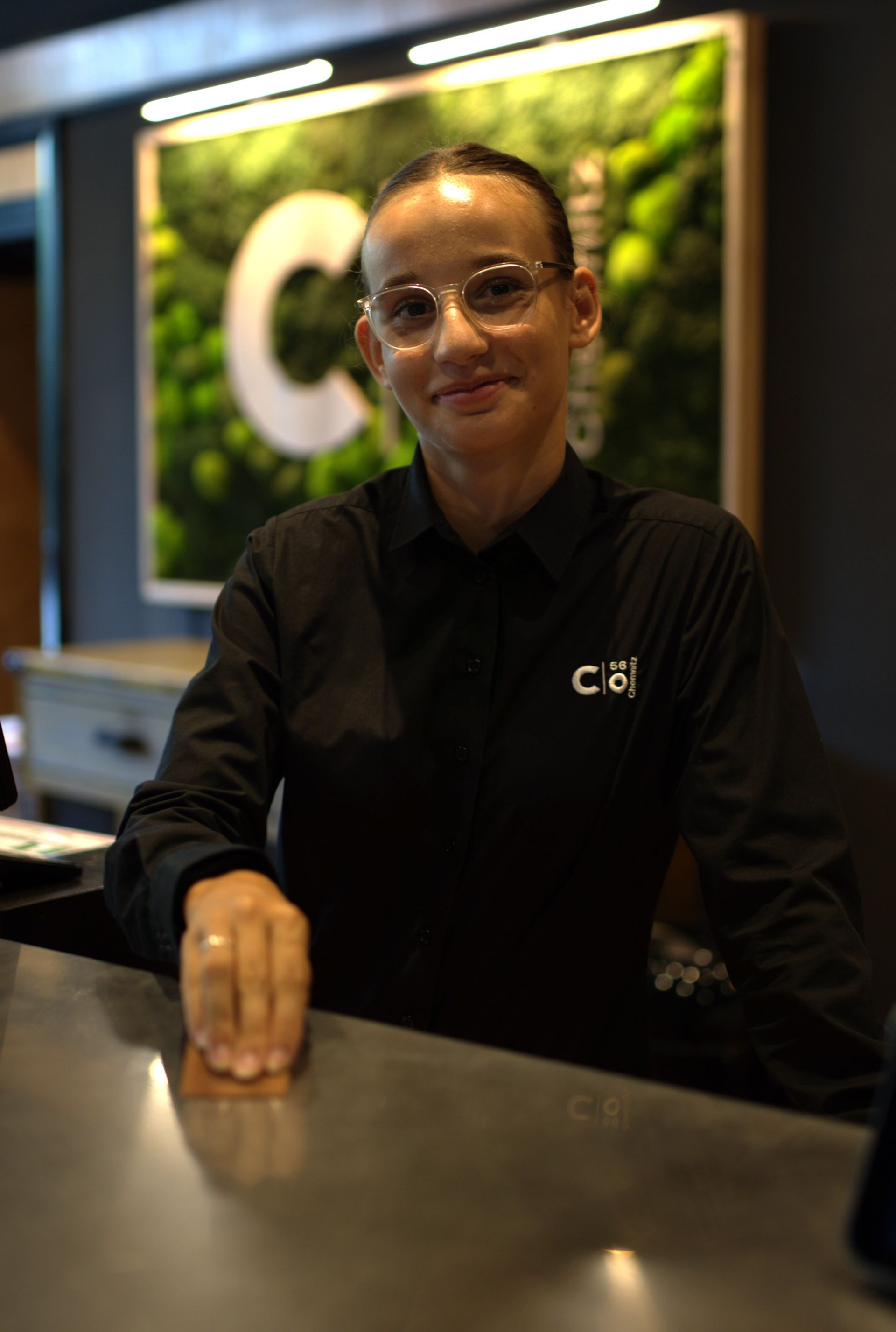 Ein lächelnder Kellner hält ein Tablett mit einem Getränk und einer Wasserflasche in einem Restaurant.