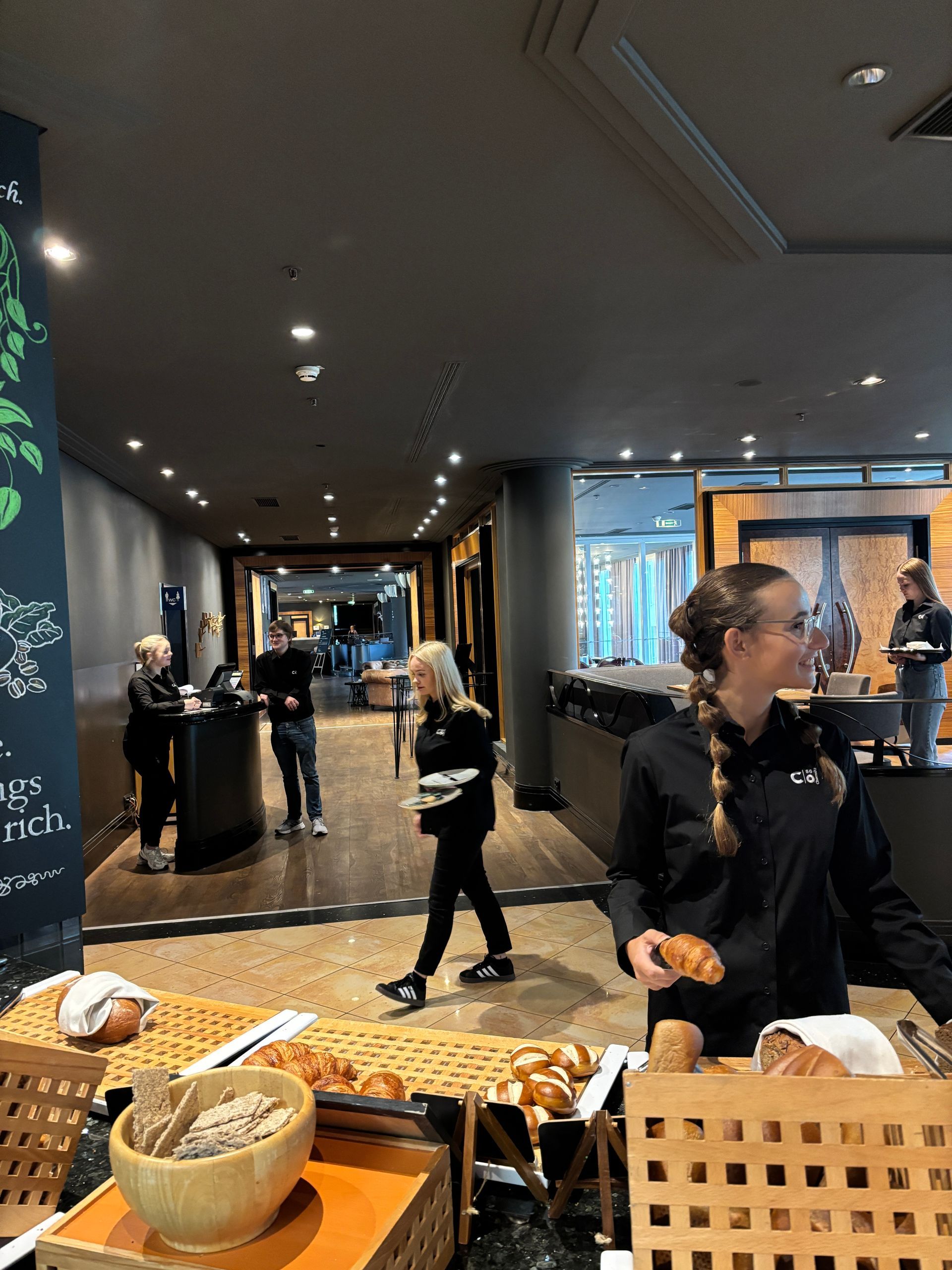 Ein lächelnder Kellner hält in einem Restaurant ein Tablett mit einem Getränk, einer Wasserflasche und einem Glas.