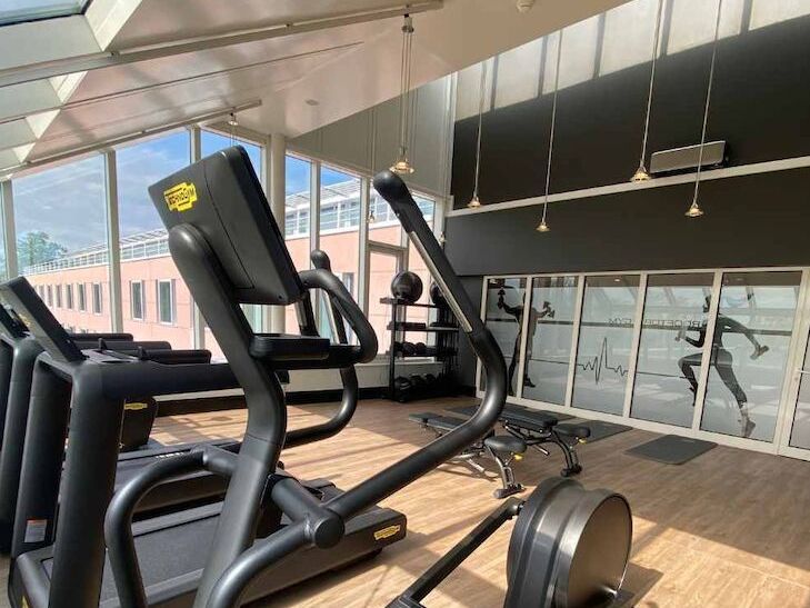 Rooftop Gym Fitnessraum mit Ellipsentrainern, Gewichten und einem Wandbild einer laufenden Figur, heller Raum mit Fenstern.