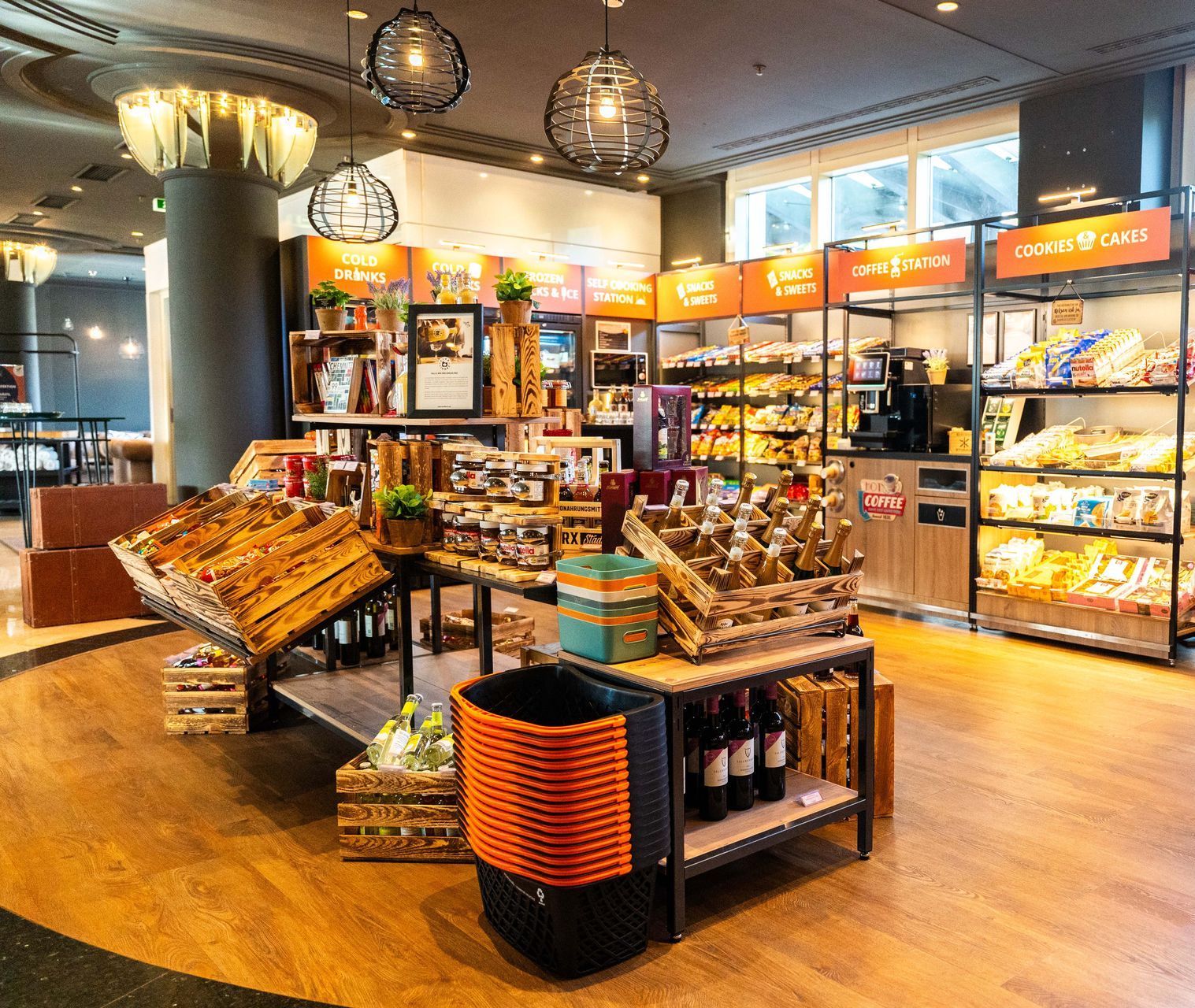 Innenansicht eines Ladens, in dem verpackte Lebensmittel, Snacks und Getränke in Regalen und Holzkisten präsentiert werden.