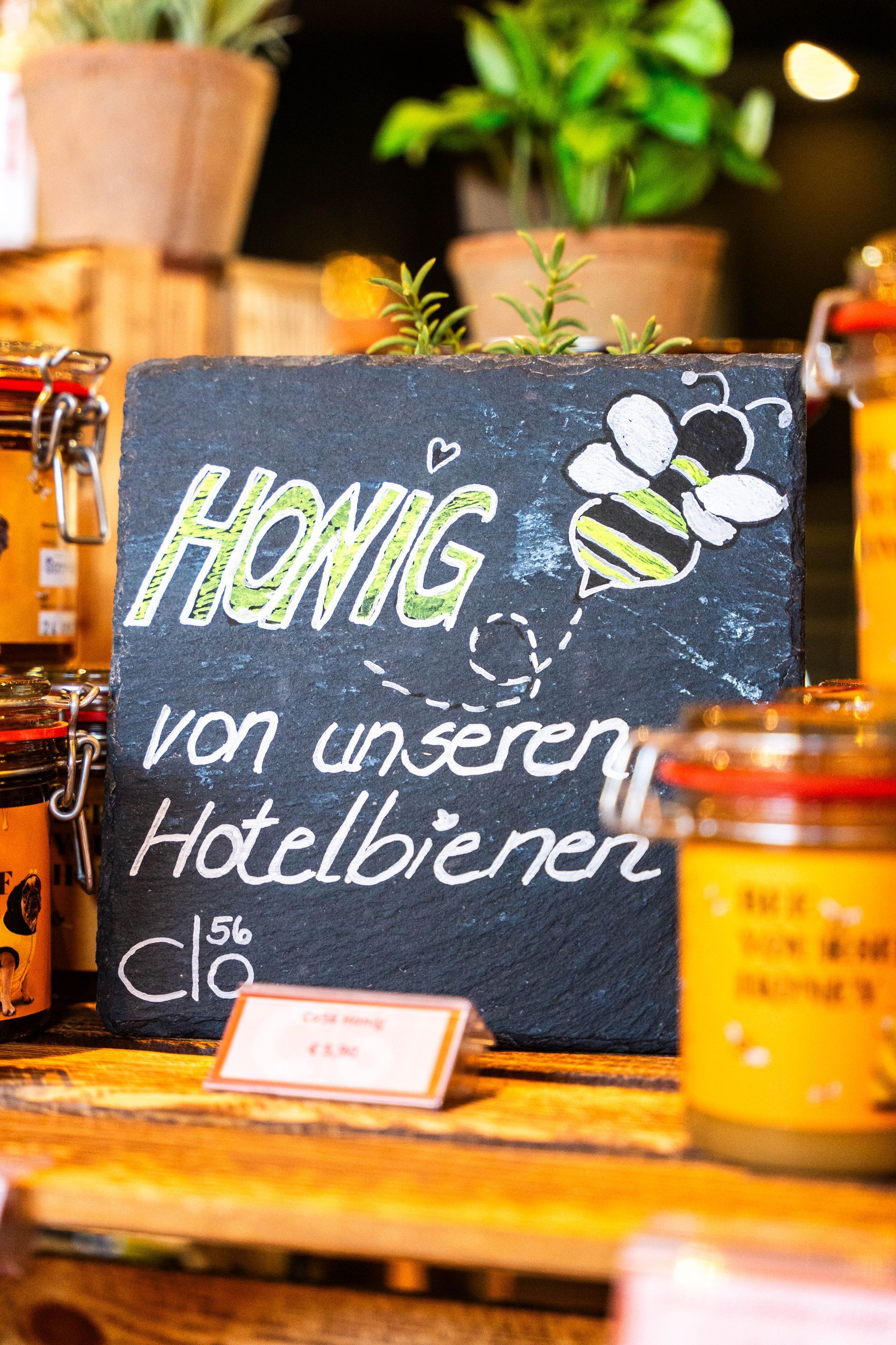 Schwarze Kreidetafel mit der Aufschrift „Honig“, einer Bienenzeichnung und Honiggläsern.