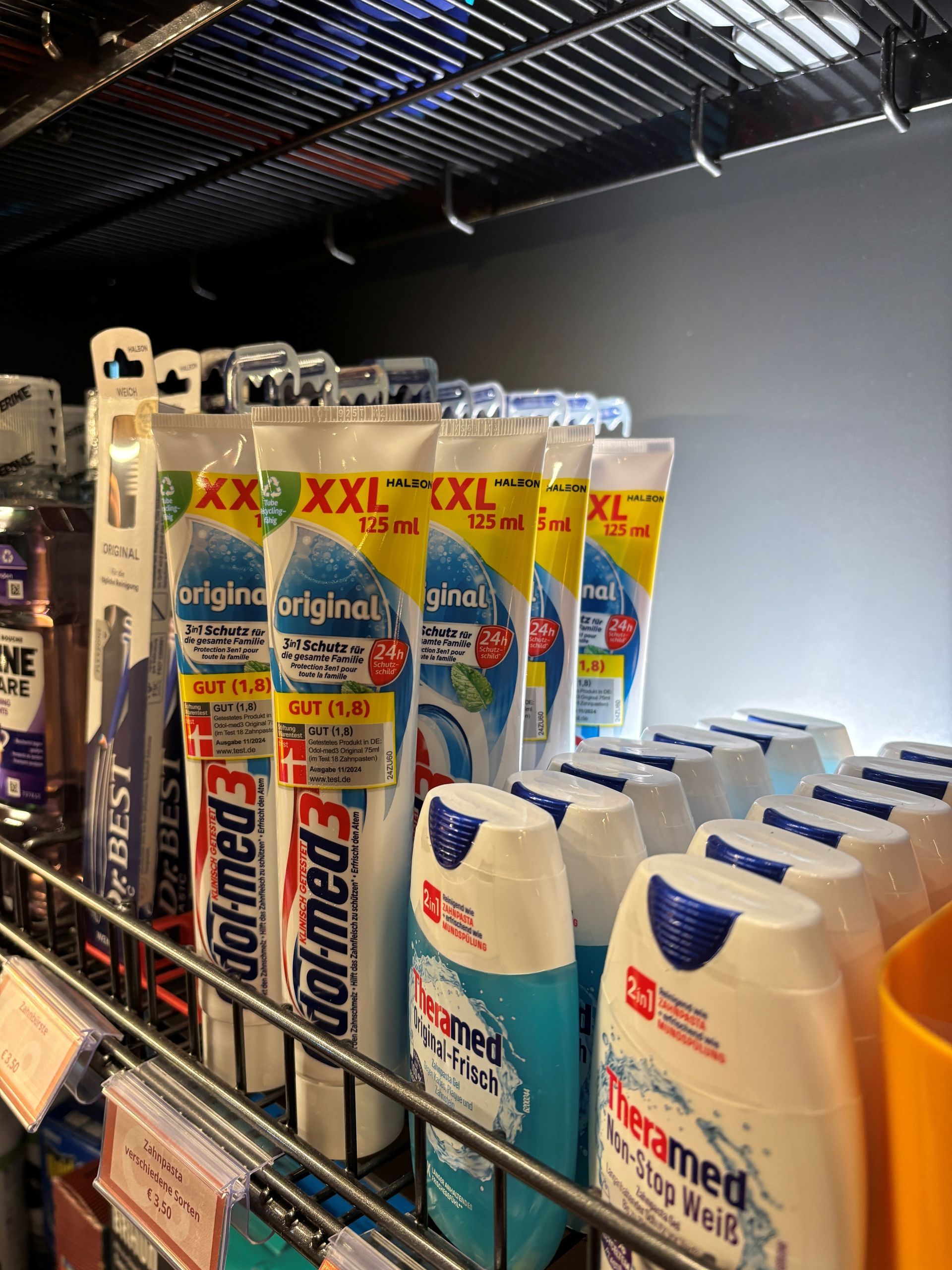Zahnpasta und Mundwasser in einem Ladenregal, wobei extra große Zahnpastatuben und blaue Mundwasserflaschen zu sehen sind.