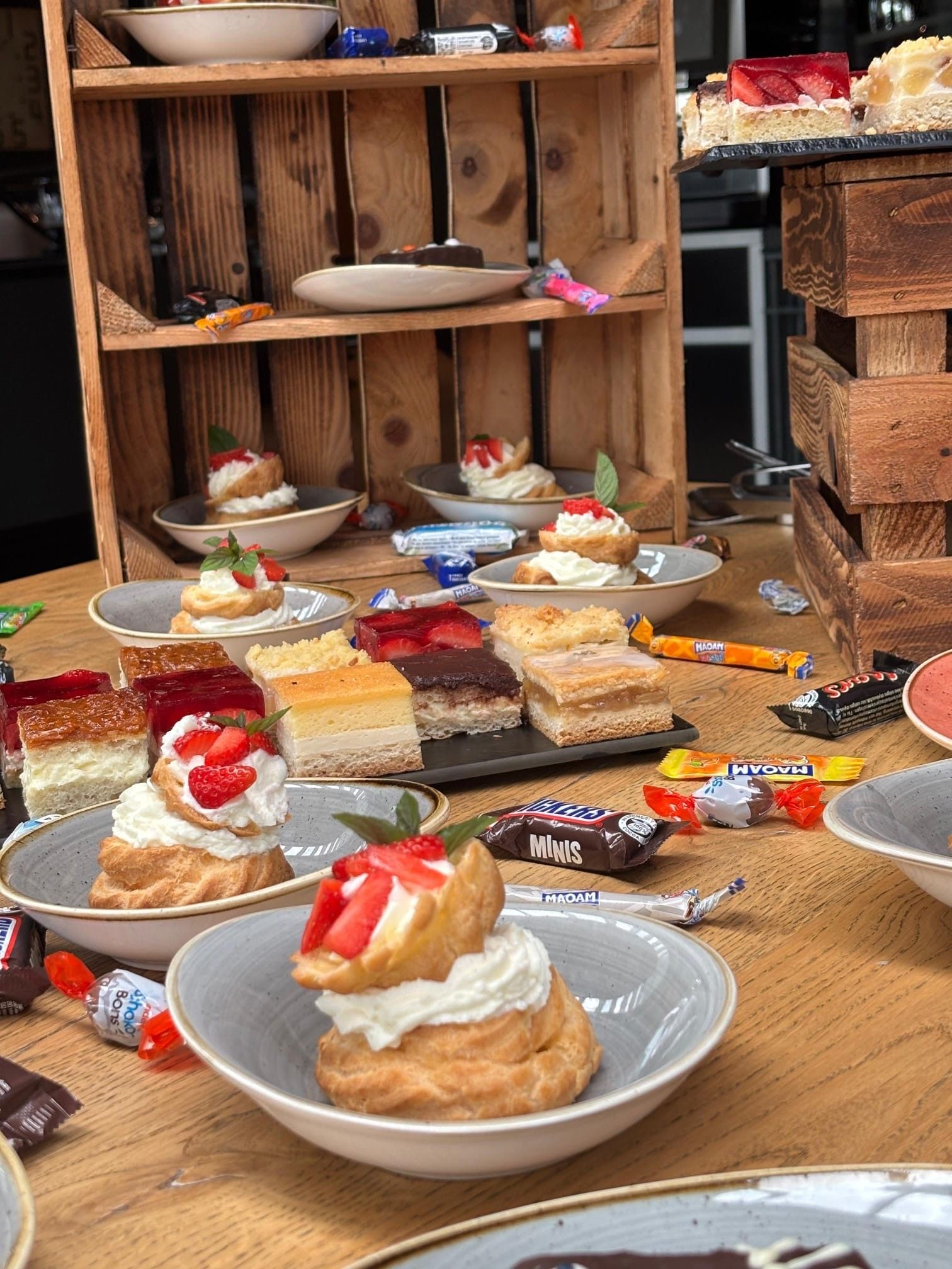 Auf Holztisch wurden Desserts ausgestellt, darunter Gebäck mit Schlagsahne und Erdbeeren, Bonbons und verschiedene Kuchen.