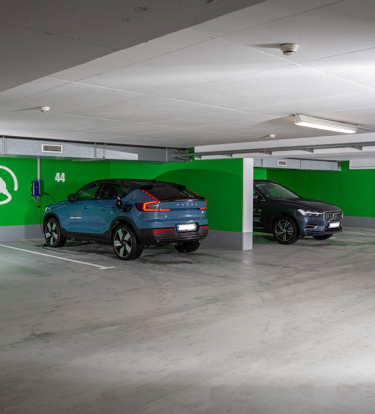 Zwei Elektroautos parken in einer leuchtend grünen Ladestation in einer Tiefgarage.