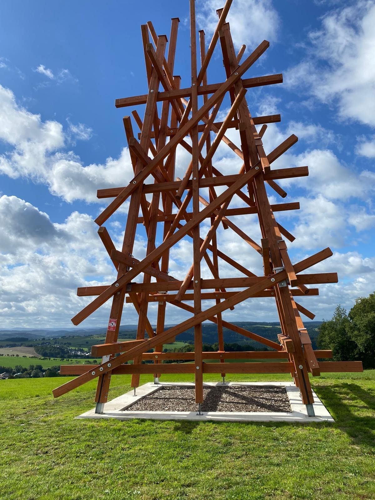 Hohe, abstrakte Holzskulptur auf einer grasbewachsenen Wiese.