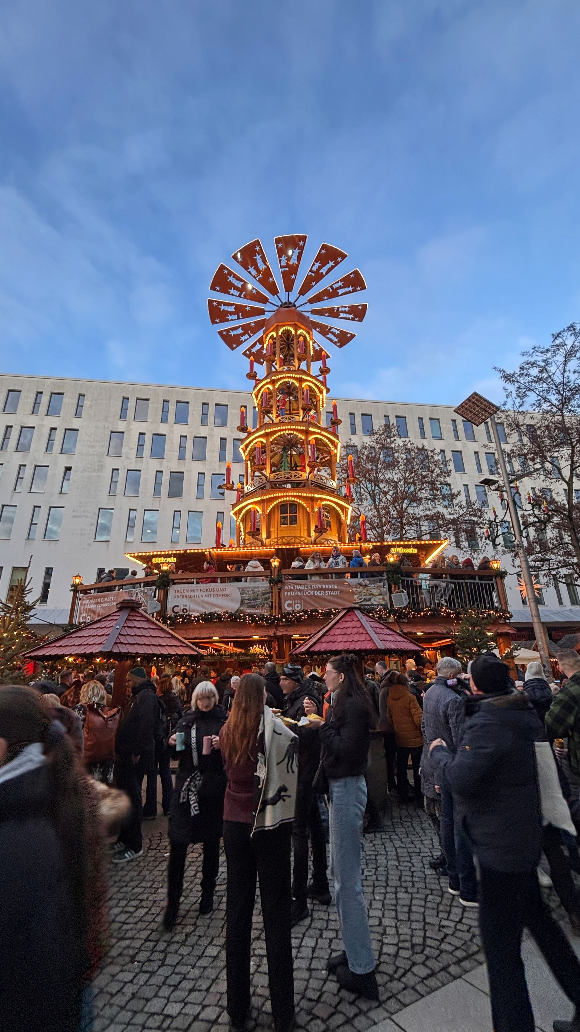 Luftaufnahme einer Stadt mit See, Bäumen und Gebäuden. Der Himmel ist teilweise bewölkt.