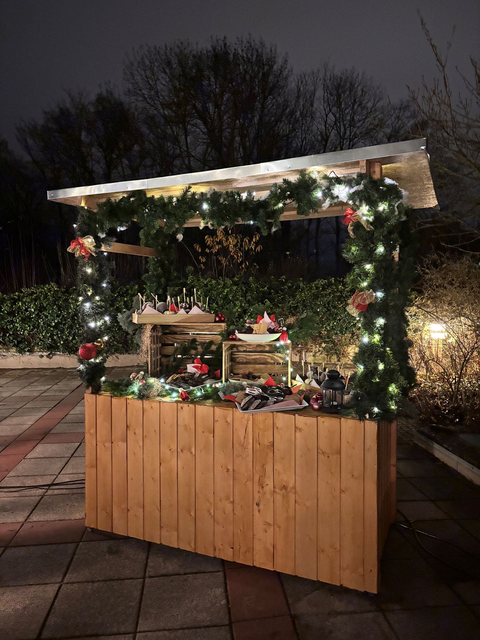 Ein hölzerner Weihnachtsmarktstand, der nachts mit Girlanden und Lichtern geschmückt ist.