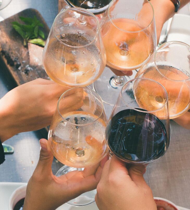 Hände, die Gläser mit verschiedenen Weinen zum Anstoßen hochhalten.