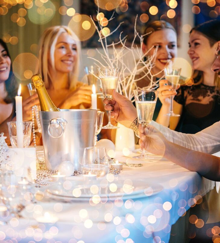 Frauen stoßen mit Champagner an einem Tisch an, der mit Lichtern und Dekorationen geschmückt ist – vermutlich eine Feier.