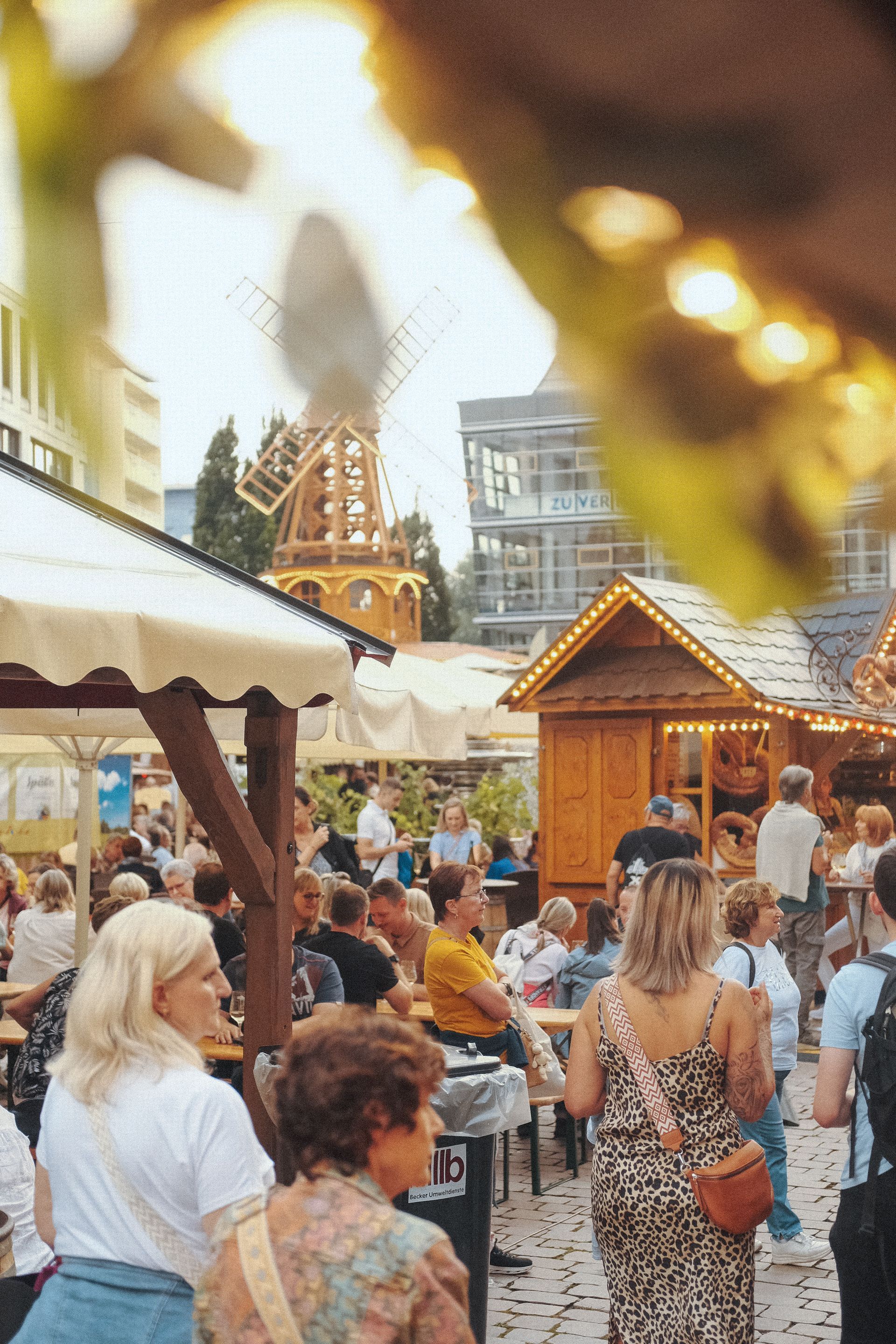 Menschenmenge auf einem Open-Air-Festival mit Holzständen und einem hohen, dekorativen, sich drehend