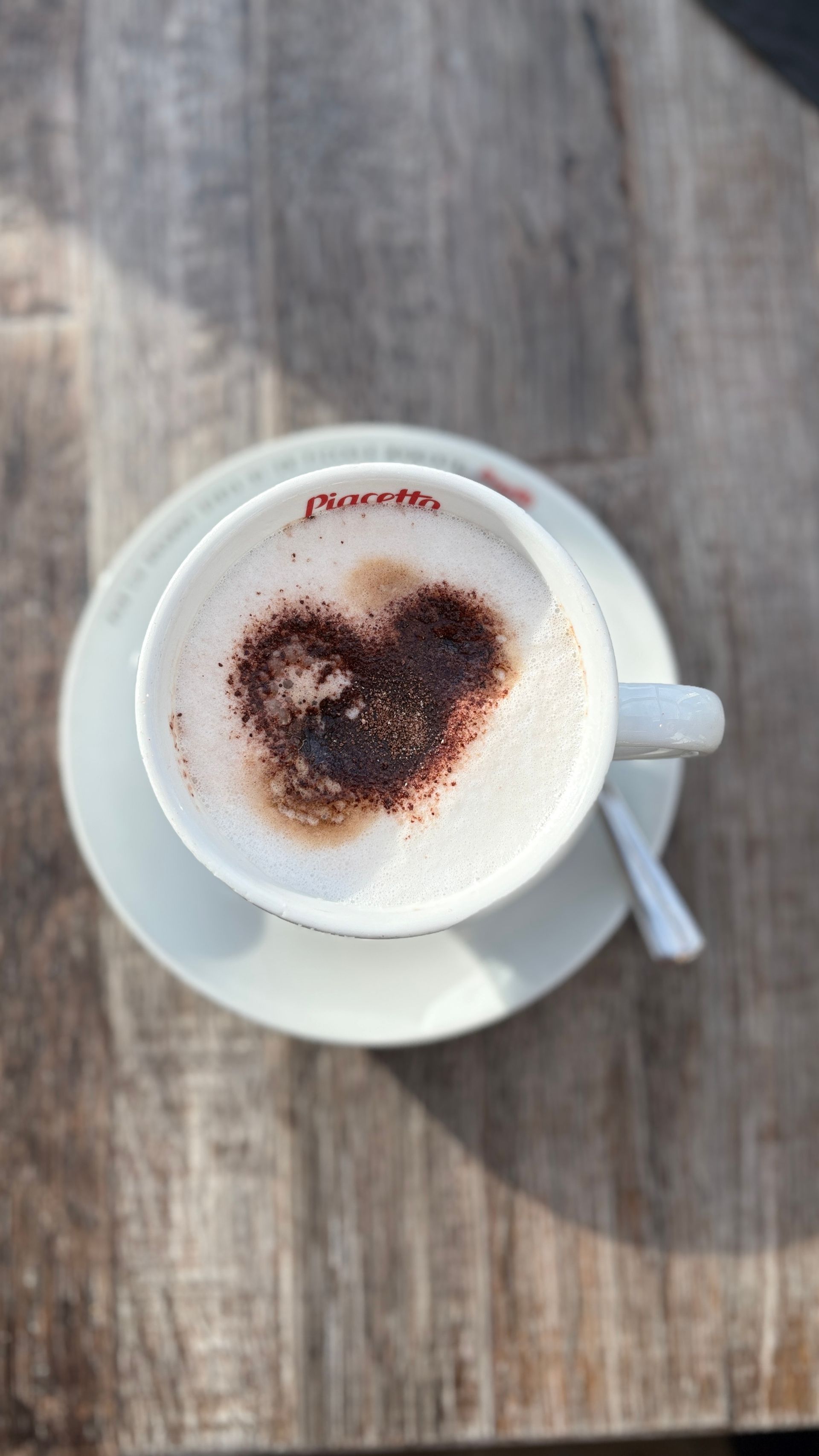 Draufsicht auf einen Cappuccino mit herzförmigem Kakaoschaum auf einer weißen Untertasse, auf einem Holztisch.