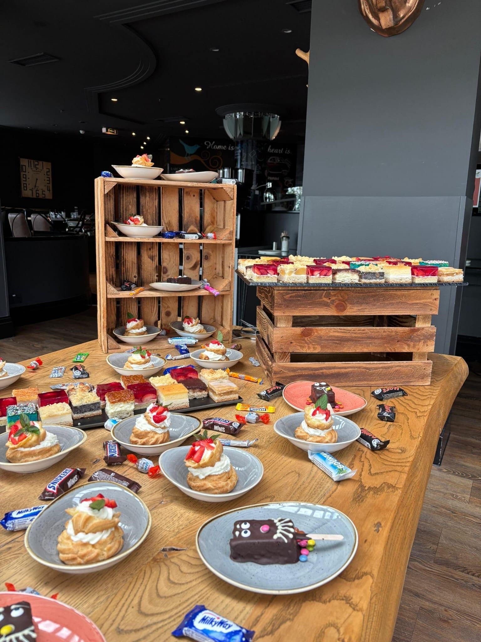 Ein Tisch mit Windbeuteln, kleinen Kuchen und verschiedenen Süßigkeiten, die auf Holzkisten und Tellern arrangiert sind.